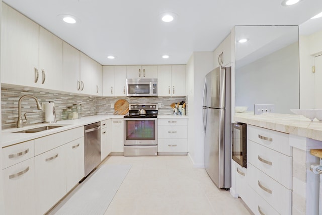 kitchen featuring tasteful backsplash, sink, light tile patterned flooring, white cabinetry, and appliances with stainless steel finishes