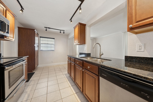 kitchen featuring dark stone counters, track lighting, sink, light tile patterned floors, and stainless steel appliances