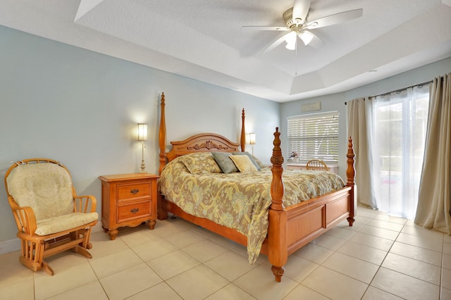 bedroom featuring ceiling fan, a tray ceiling, light tile patterned floors, and a textured ceiling