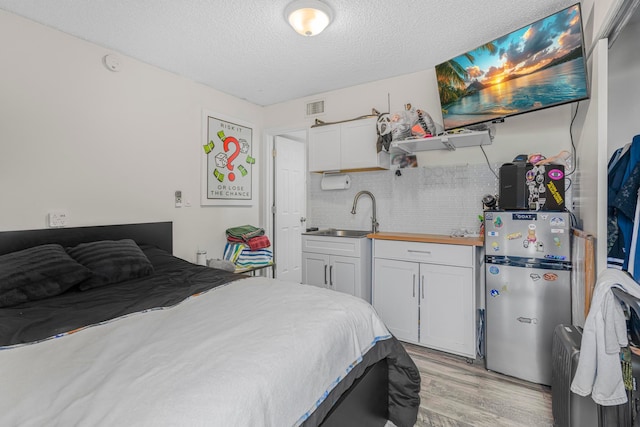 bedroom with a textured ceiling, stainless steel refrigerator, sink, and light wood-type flooring