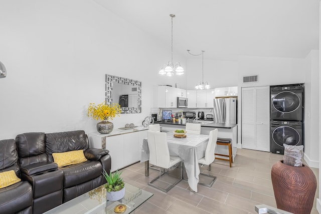 dining space featuring a notable chandelier, stacked washer and clothes dryer, and high vaulted ceiling