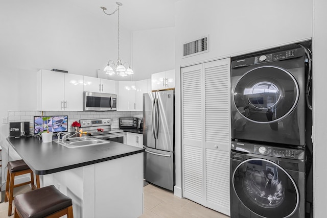 kitchen featuring kitchen peninsula, hanging light fixtures, white cabinetry, stacked washer and dryer, and stainless steel appliances