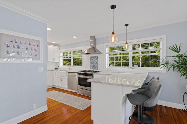 kitchen featuring appliances with stainless steel finishes, light stone counters, wall chimney exhaust hood, white cabinets, and hardwood / wood-style floors