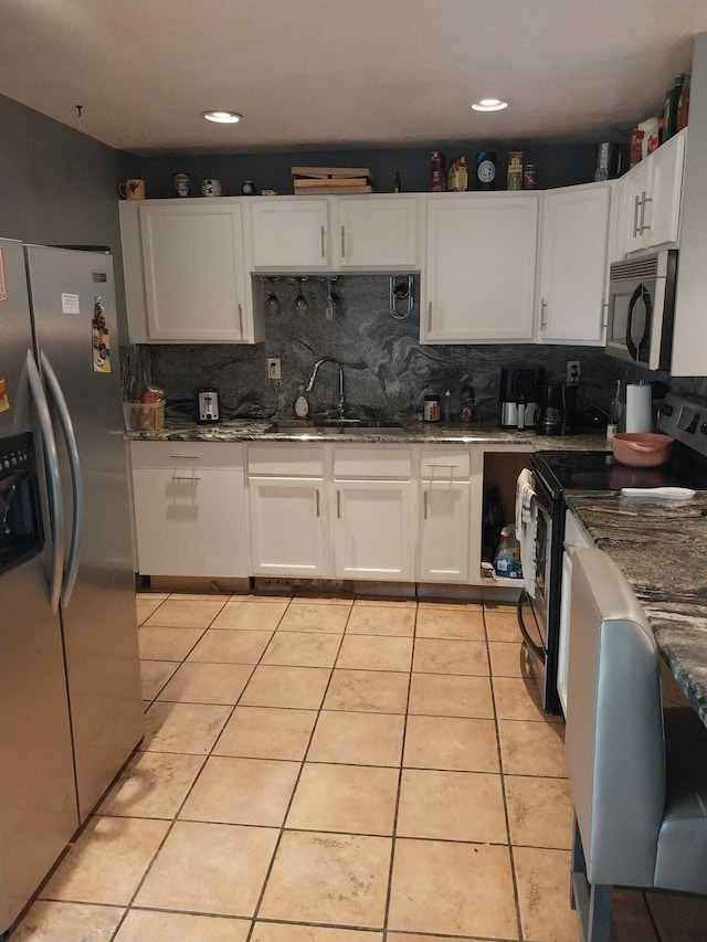 kitchen with dark stone countertops, appliances with stainless steel finishes, light tile patterned floors, and white cabinetry