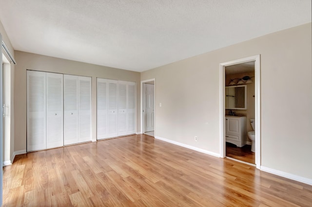 unfurnished bedroom with light wood-type flooring, sink, connected bathroom, multiple closets, and a textured ceiling