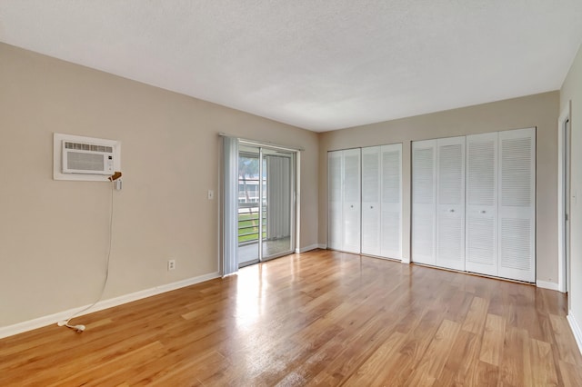 unfurnished bedroom with a textured ceiling, light hardwood / wood-style flooring, two closets, access to exterior, and an AC wall unit