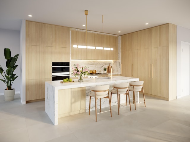 kitchen with double oven, light brown cabinets, a kitchen island with sink, a breakfast bar area, and light tile patterned flooring