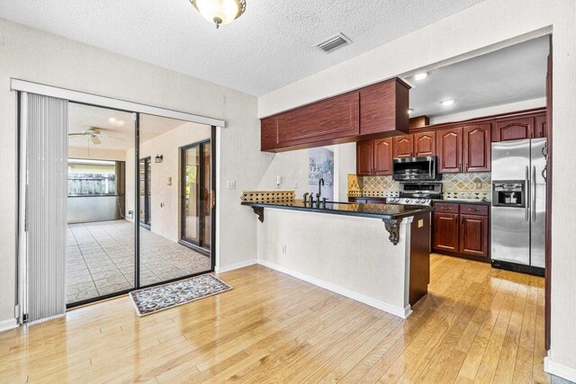 kitchen featuring stainless steel appliances, backsplash, kitchen peninsula, light hardwood / wood-style floors, and a kitchen bar