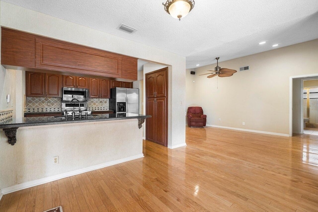 kitchen with sink, light wood-type flooring, appliances with stainless steel finishes, tasteful backsplash, and kitchen peninsula