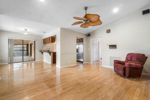 living room featuring a textured ceiling, ceiling fan, lofted ceiling, and light wood-type flooring