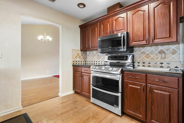 kitchen with a notable chandelier, stainless steel appliances, backsplash, light wood finished floors, and dark countertops