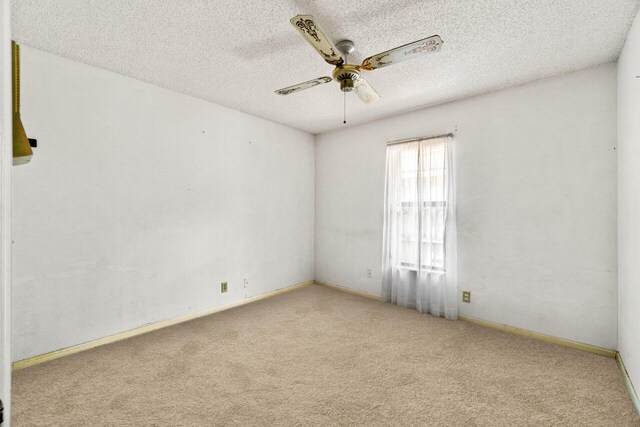 empty room with a ceiling fan, light colored carpet, a textured ceiling, and baseboards