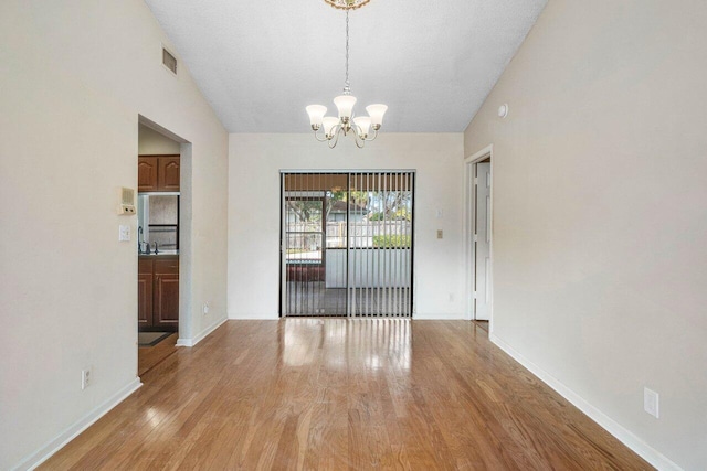 unfurnished dining area featuring vaulted ceiling, sink, light hardwood / wood-style flooring, and an inviting chandelier