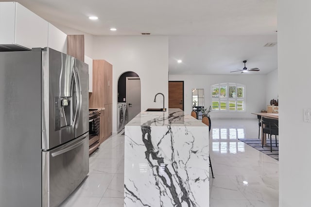 kitchen featuring light stone countertops, an island with sink, stainless steel appliances, white cabinets, and washer and clothes dryer