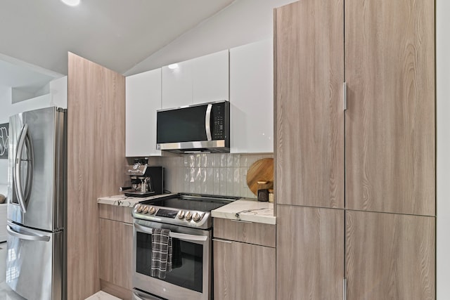 kitchen with lofted ceiling, white cabinets, decorative backsplash, appliances with stainless steel finishes, and light stone counters