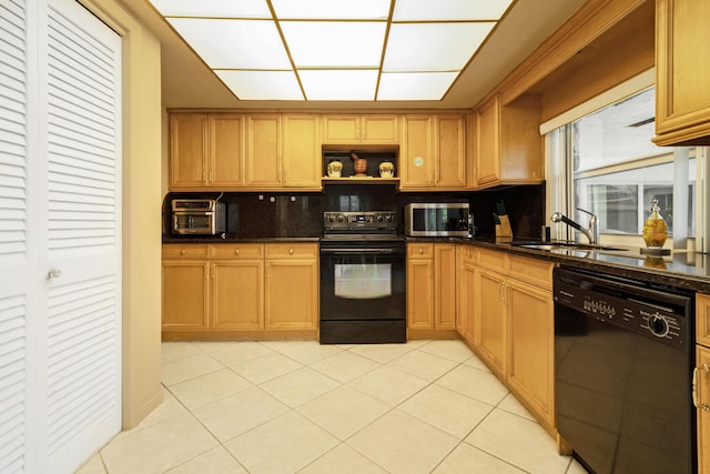 kitchen with backsplash, black appliances, sink, light tile patterned floors, and dark stone counters