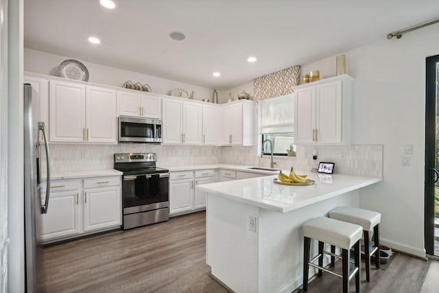 kitchen featuring kitchen peninsula, white cabinets, wood-type flooring, and appliances with stainless steel finishes