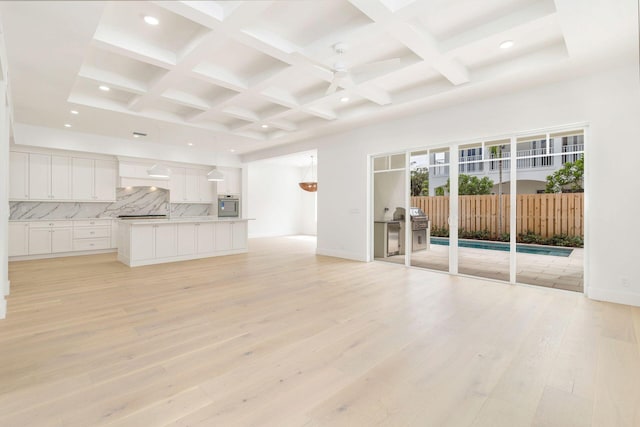 unfurnished living room featuring light wood-style floors, ceiling fan, beamed ceiling, and coffered ceiling