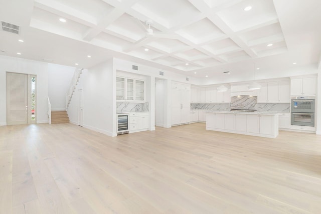 unfurnished living room featuring wine cooler, beamed ceiling, coffered ceiling, and light hardwood / wood-style floors