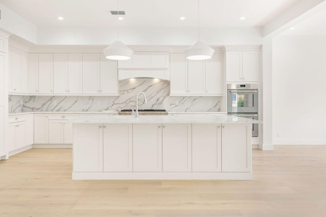 kitchen featuring stainless steel double oven, visible vents, tasteful backsplash, a center island with sink, and white cabinetry