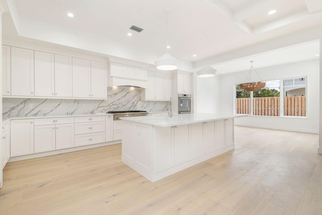kitchen featuring decorative backsplash, a kitchen island with sink, appliances with stainless steel finishes, light wood-style floors, and white cabinetry