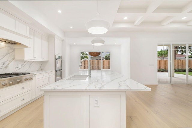 kitchen featuring white cabinets, hanging light fixtures, an island with sink, light hardwood / wood-style floors, and sink