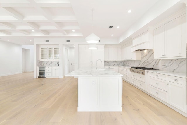 kitchen with light hardwood / wood-style floors, decorative backsplash, stainless steel gas stovetop, and a center island with sink