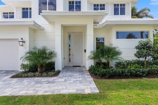 doorway to property with a garage, stucco siding, and a lawn