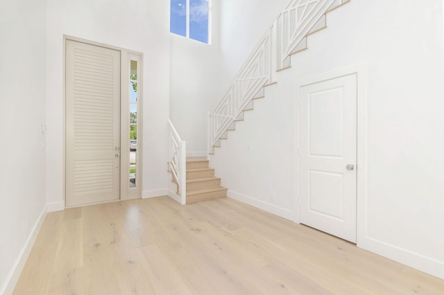 entrance foyer with light wood-type flooring, baseboards, a high ceiling, and stairway