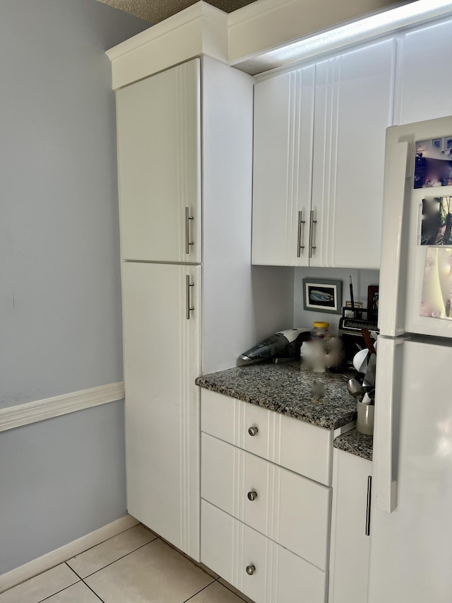 kitchen with dark stone countertops, white cabinetry, light tile patterned flooring, and white refrigerator