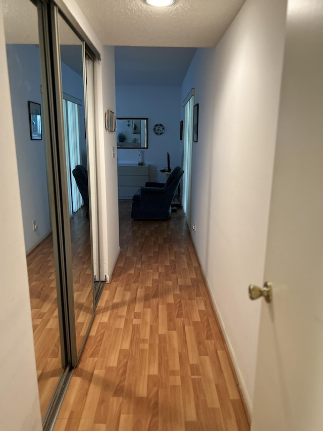 corridor with light wood-style flooring, a textured ceiling, and baseboards