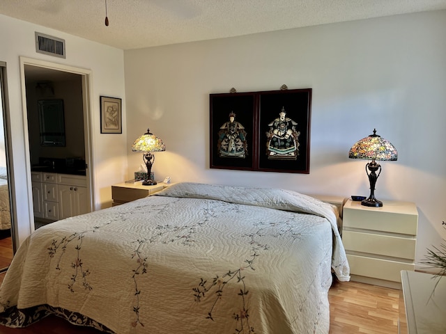 bedroom with light wood-style floors, visible vents, and a textured ceiling