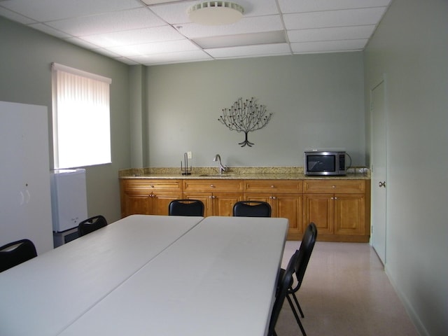 kitchen featuring a paneled ceiling, light countertops, stainless steel microwave, brown cabinetry, and a sink