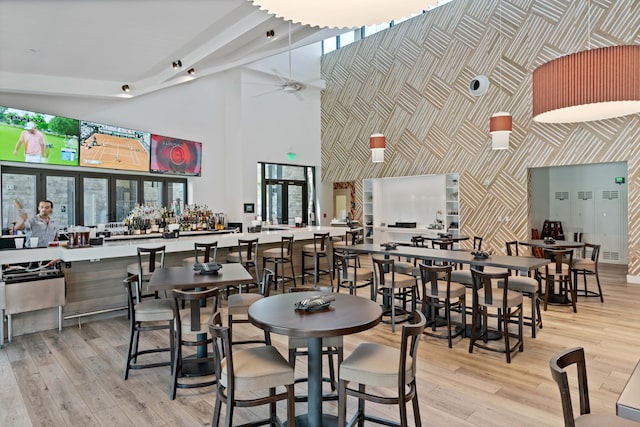 dining space with light hardwood / wood-style flooring, bar, a towering ceiling, and ceiling fan