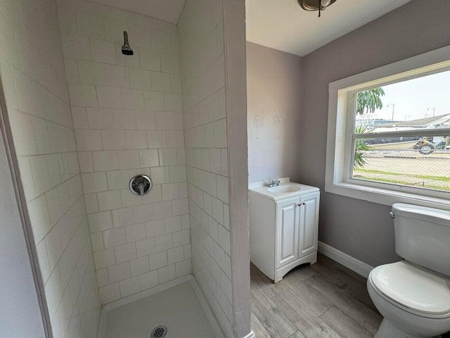 bathroom featuring baseboards, wood finished floors, toilet, and tiled shower