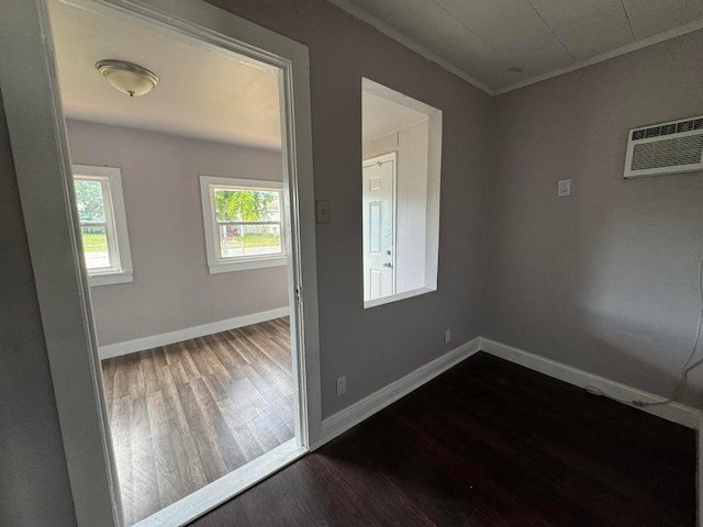 empty room featuring a wall mounted AC, ornamental molding, baseboards, and dark wood-style flooring