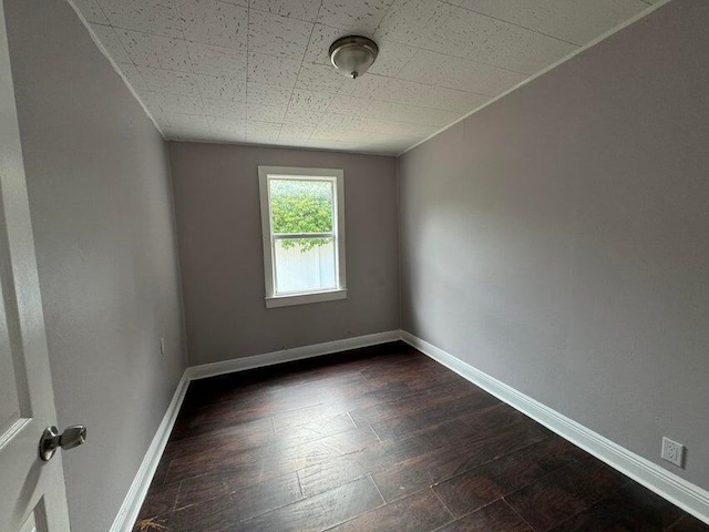 spare room featuring baseboards and dark wood-style flooring