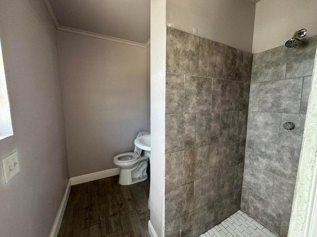 bathroom with wood finished floors, toilet, crown molding, baseboards, and tiled shower