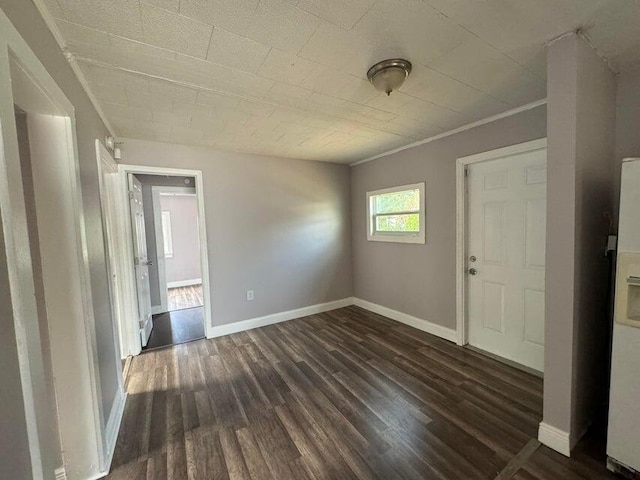 empty room with dark wood-type flooring, crown molding, and baseboards
