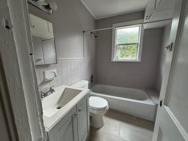 full bathroom featuring tiled shower / bath, vanity, tile patterned floors, tile walls, and toilet