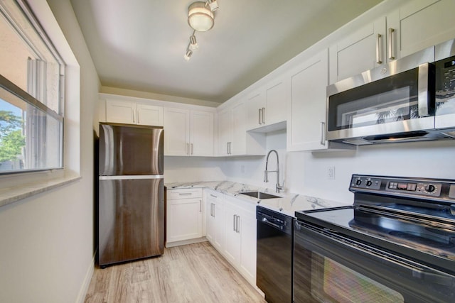 kitchen featuring light stone countertops, black appliances, sink, white cabinetry, and light hardwood / wood-style flooring