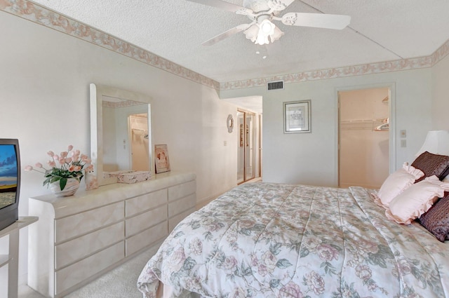 bedroom with ceiling fan, a textured ceiling, a walk in closet, a closet, and light colored carpet