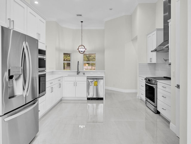 kitchen featuring crown molding, wall chimney range hood, appliances with stainless steel finishes, pendant lighting, and white cabinets