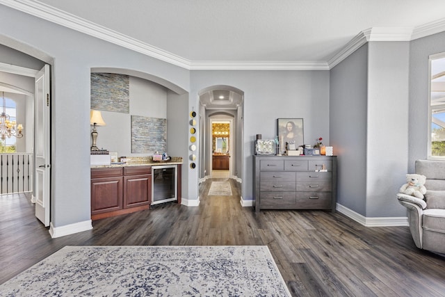 bar with beverage cooler, dark hardwood / wood-style flooring, an inviting chandelier, ornamental molding, and dark brown cabinets