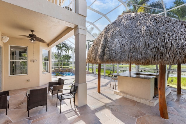 view of patio / terrace featuring glass enclosure, ceiling fan, and exterior bar