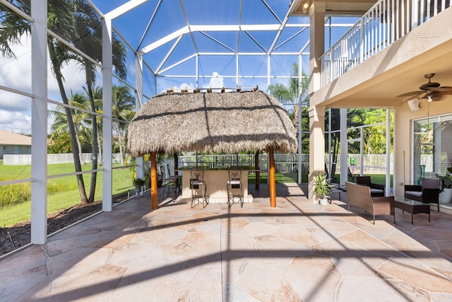 view of patio / terrace with ceiling fan, a bar, and a lanai