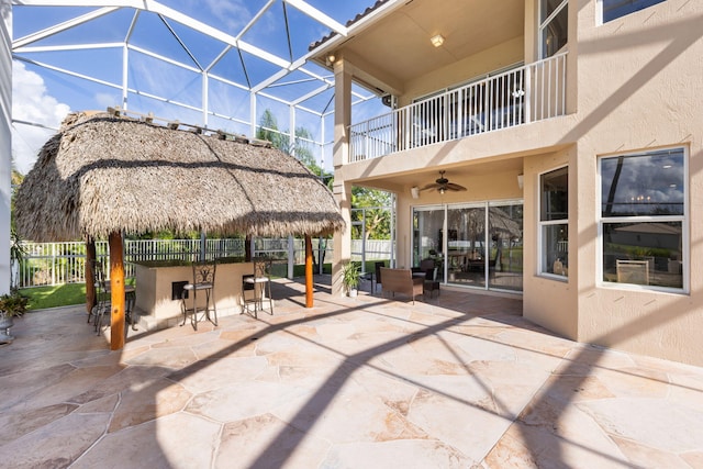 view of patio with ceiling fan, a balcony, glass enclosure, and a bar