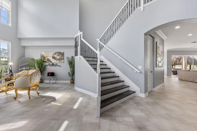 staircase featuring a towering ceiling, ceiling fan, crown molding, and a healthy amount of sunlight