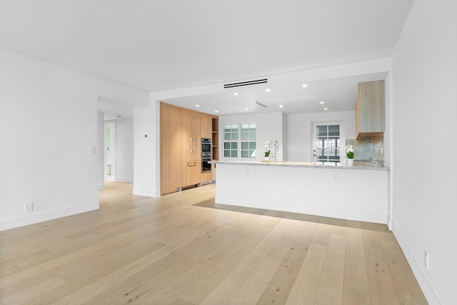 interior space featuring double oven, light stone counters, kitchen peninsula, light brown cabinets, and light wood-type flooring