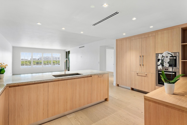 kitchen featuring light wood-type flooring, stainless steel double oven, sink, and light brown cabinets